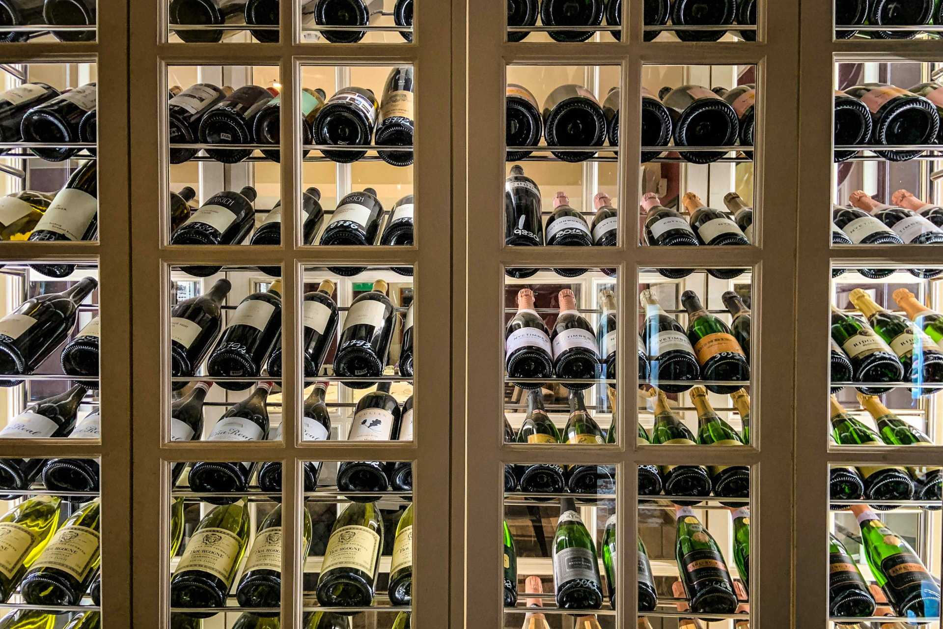 A backlit wall of wine bottles in wooden cellar racking.