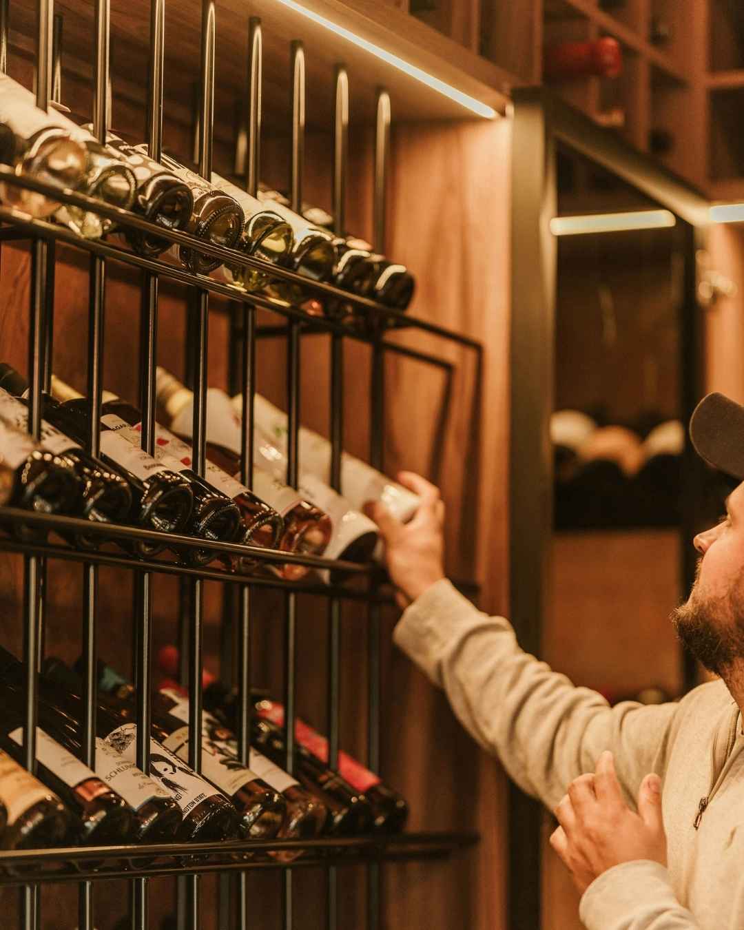 A sommelier selecting a bottle from a backlit cellar rack.